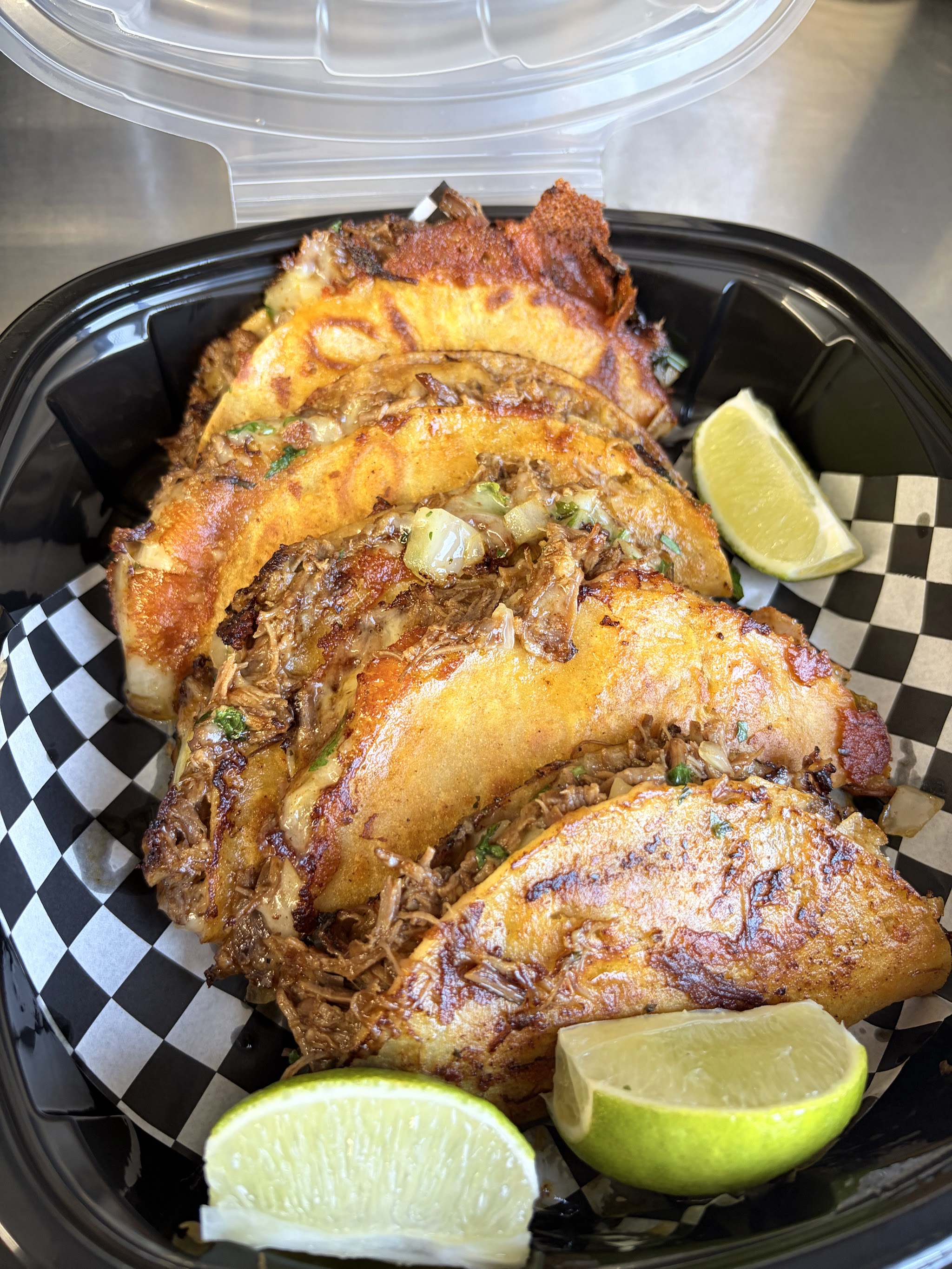 Crispy birria quesitacos in a black tray with lime wedges