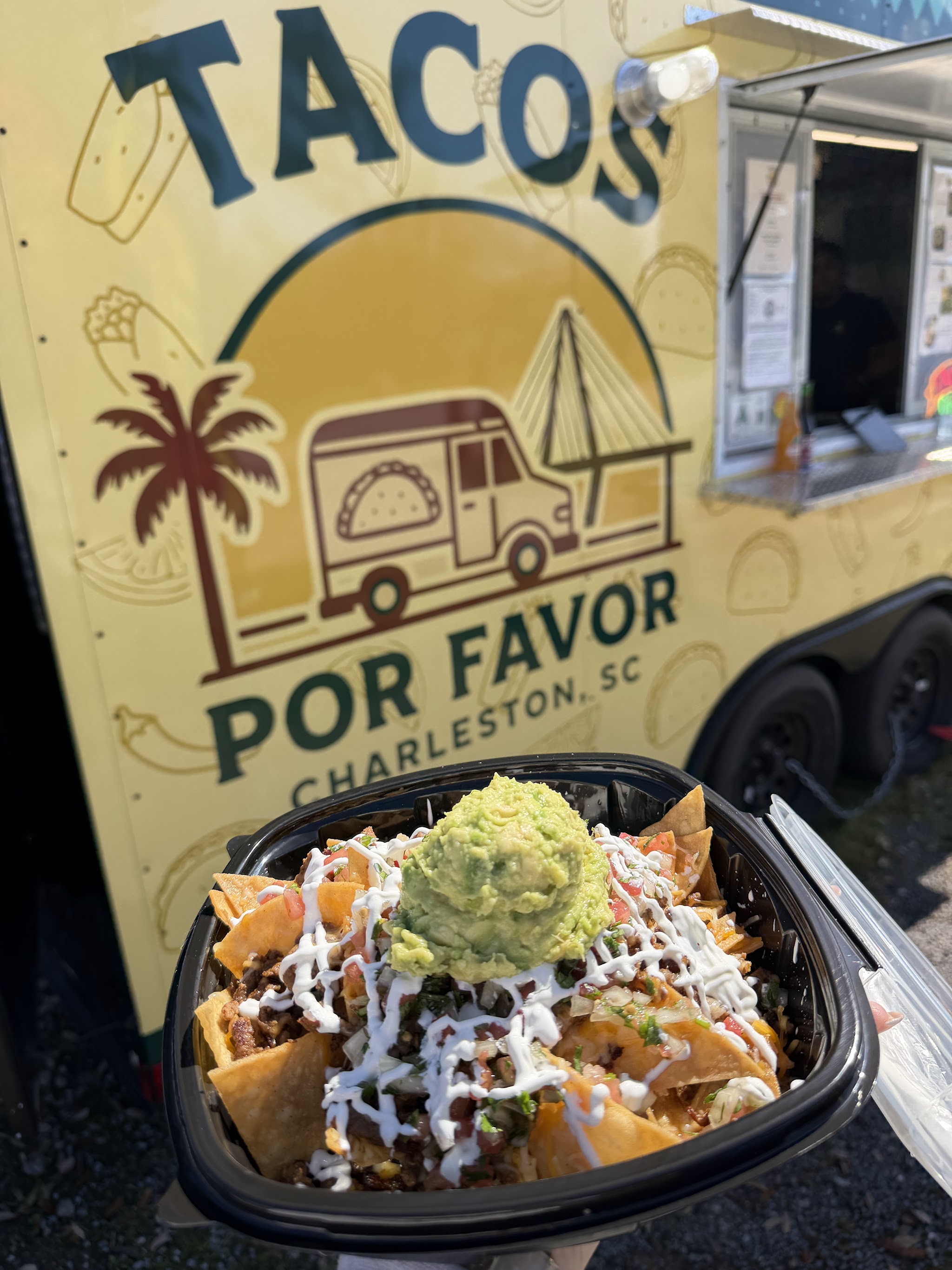 Loaded nachos topped with guacamole and crema in front of our truck logo