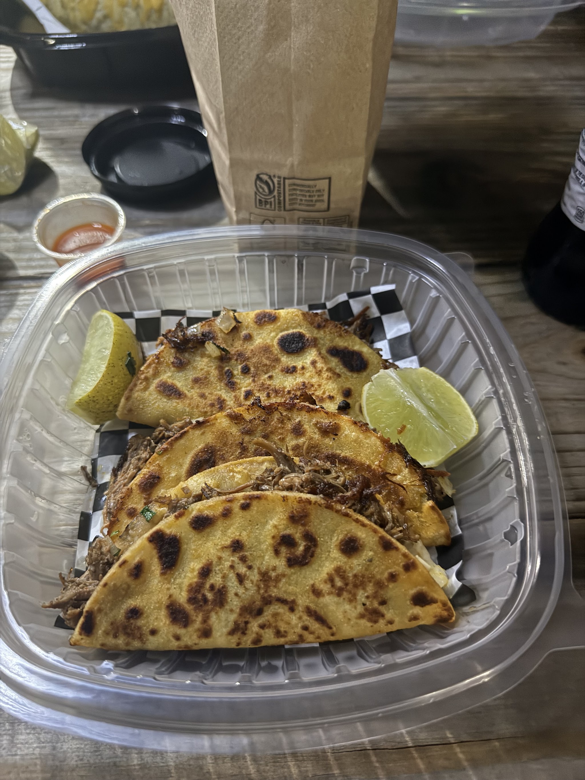 Three birria tacos in a clear container with lime