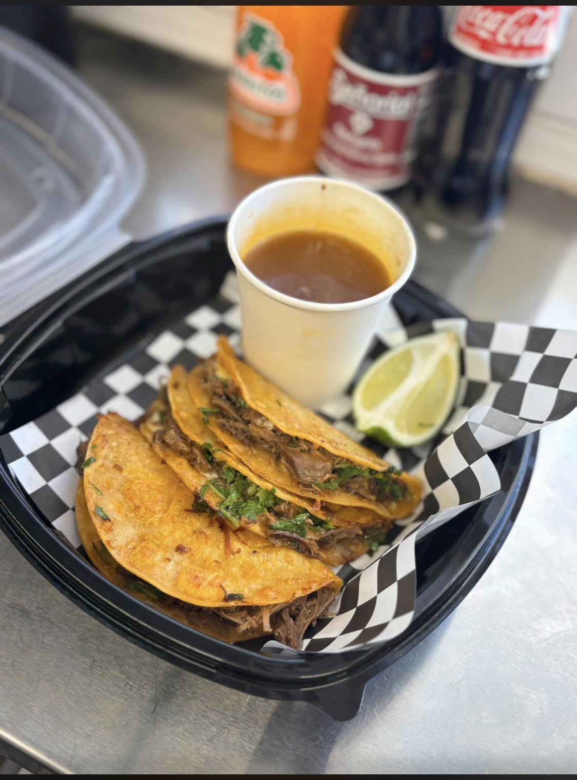 Birria tacos with a cup of consomé and Mexican sodas